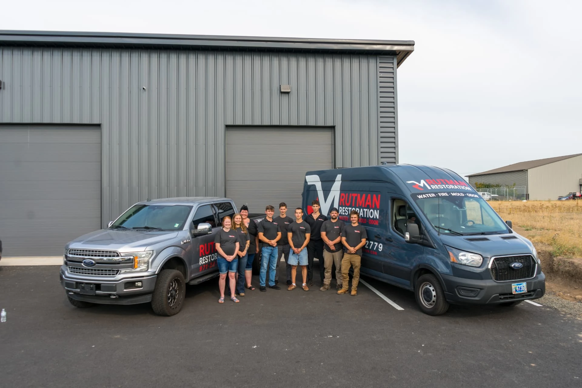 Historical Rutman Restoration team standing between the branded truck and restoration van outside a commercial building in Oregon